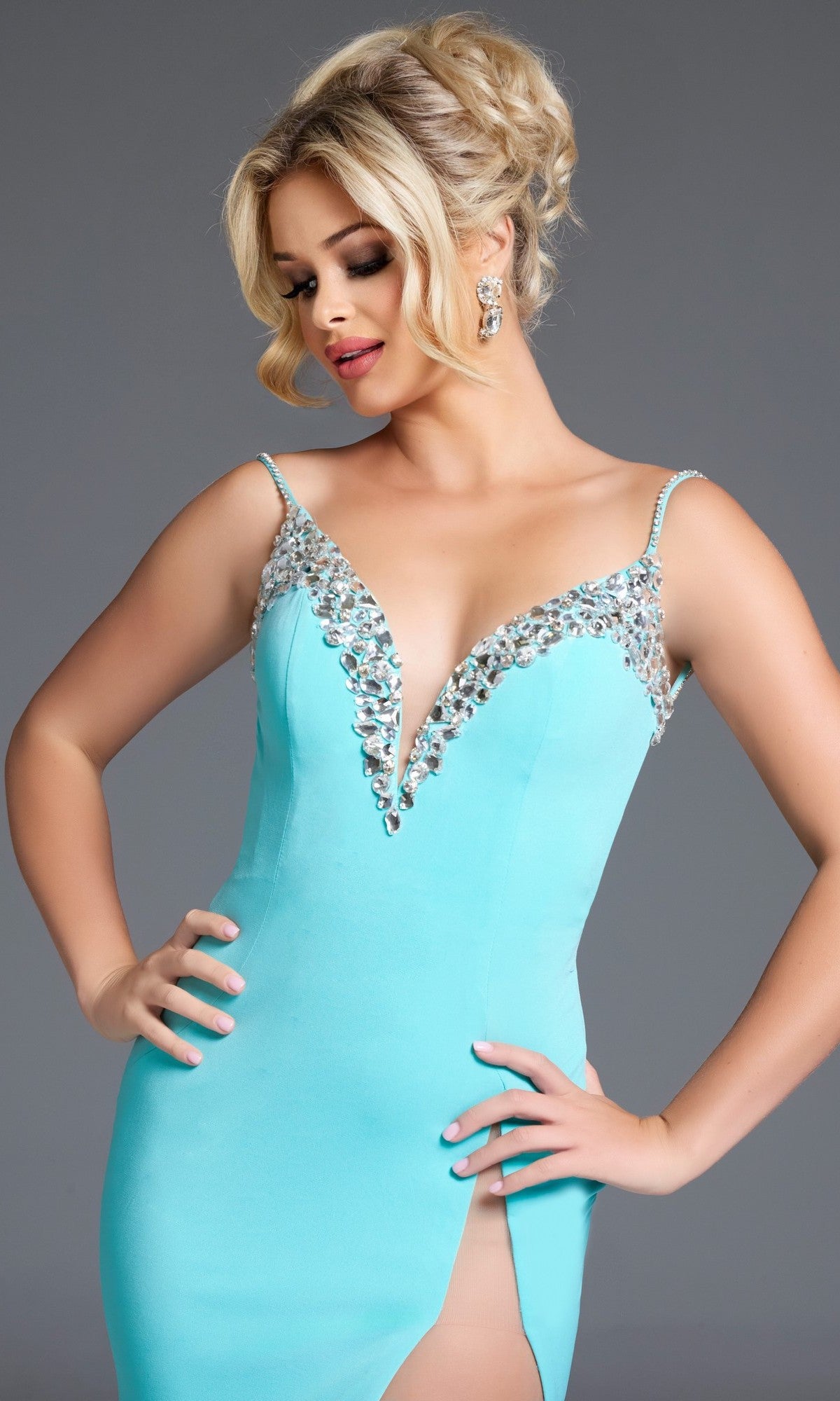 Woman wearing Jovani 38989, a light blue long prom dress featuring a beaded neckline and thigh-high slit, poses with hands on hips against a plain gray background.